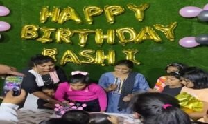 A group of children celebrating a birthday with balloons and a cake, featuring the text 'Happy Birthday Rashi' in gold letters.
